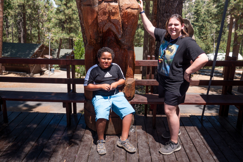 A young male camper and a male camp counselor posing in front of a wooden bear statue