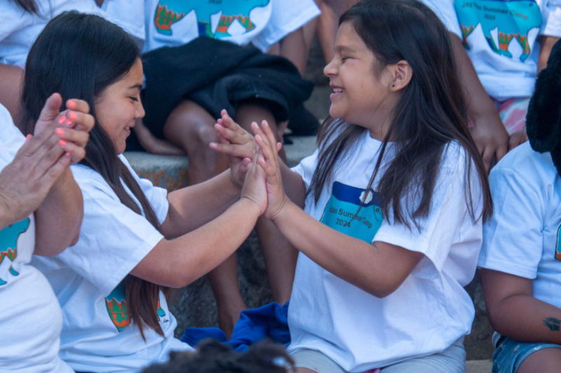 Two girls playing patty cake while wearing white camp t-shirts during a group photoshoot