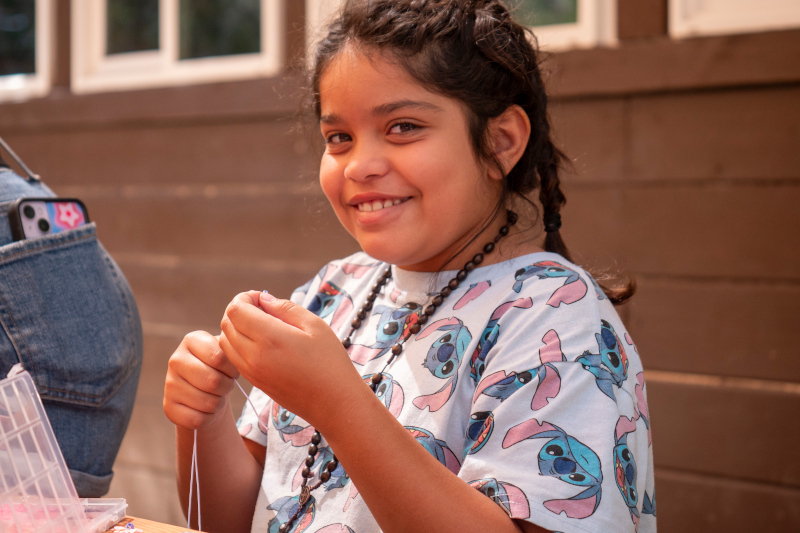 Girl wearing a lilo and stitch t-shirt making a beaded bracelet 