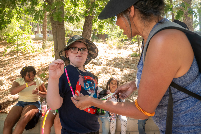 A camp counselor helping out a young camper with disabilities with his beaded bracelet.