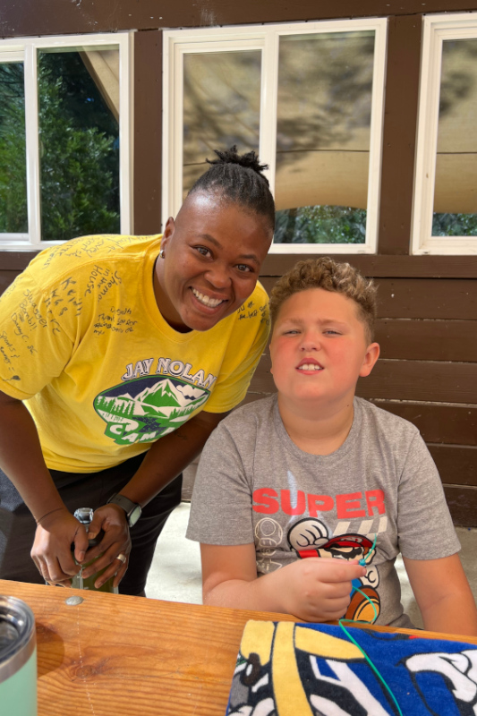 Camp director wearing a yellow camp t-shirt posing with a male camper wearing a grey t-shirt