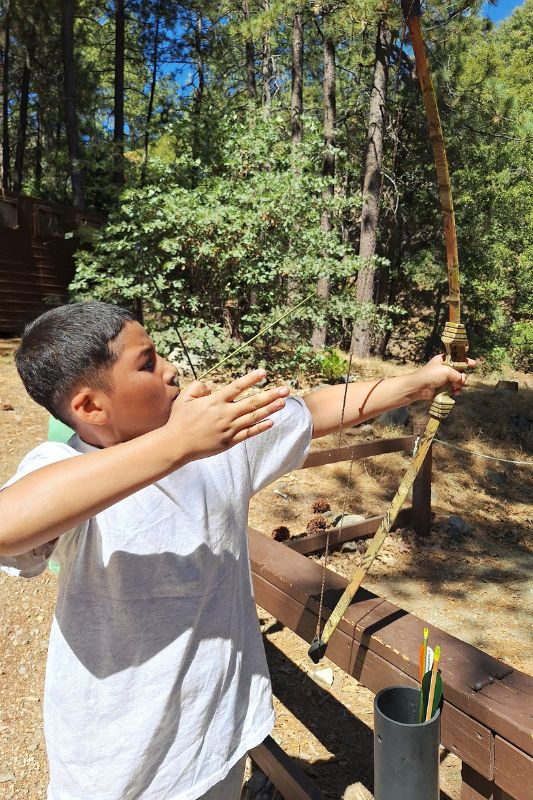 Boy in a white t-shirt shooting a bow and arrow