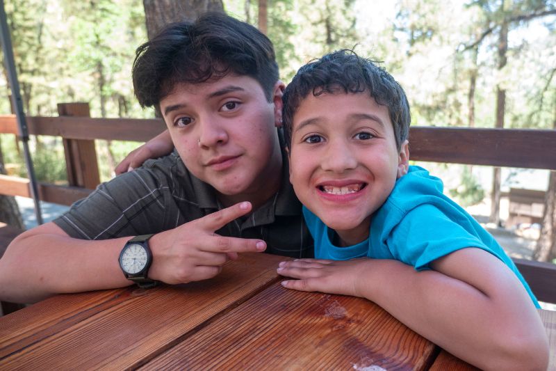 Two Latino boys posing together and smiling at a picnic bench.