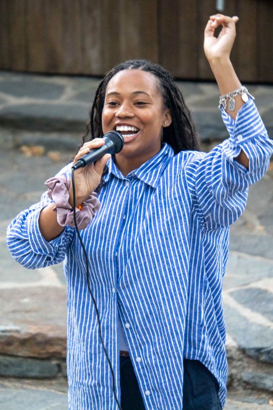 Camp theater coordinator, a young African American woman in a blue striped blouse, speaking into a microphone.